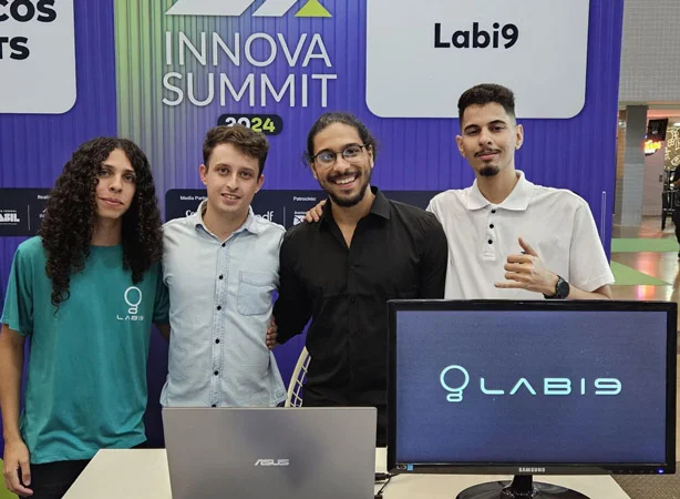 Nesta imagem, vemos um grupo de pessoas ao lado de um computador. Os homems usam óculos e relógio. O grupo está reunido em torno de um laptop, com uma pessoa ao lado dele. Os indivíduos parecem estar envolvidos com o computador, possivelmente discutindo algo na tela. O cenário parece ser um ambiente casual e colaborativo. A imagem também mostra um monitor/TV ao fundo. As pessoas estão vestidas casualmente e uma pessoa está sorrindo. A atmosfera geral é de trabalho em equipe e uso de tecnologia. #EquipeTop #TrabalhoEmEquipe #EmpresaUnida